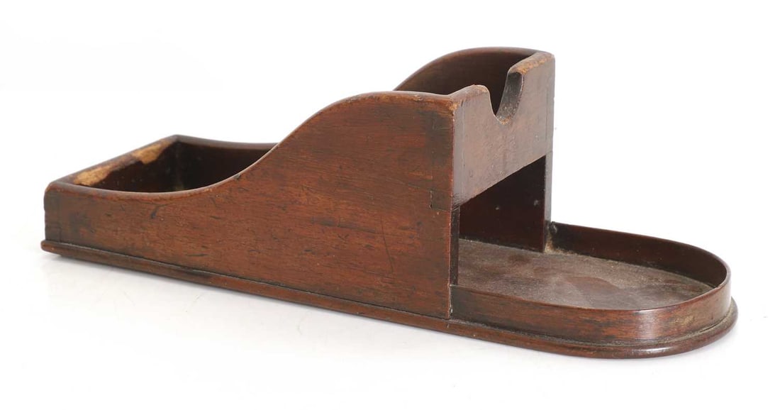 A mahogany wine bottle stand, 19th century,: A mahogany wine bottle stand, 19th century, with shaped sides 34cm wide, 12cm deep, 11cm high Condition Report: Knocks and wear with loss to the edges, wear and watermarks.