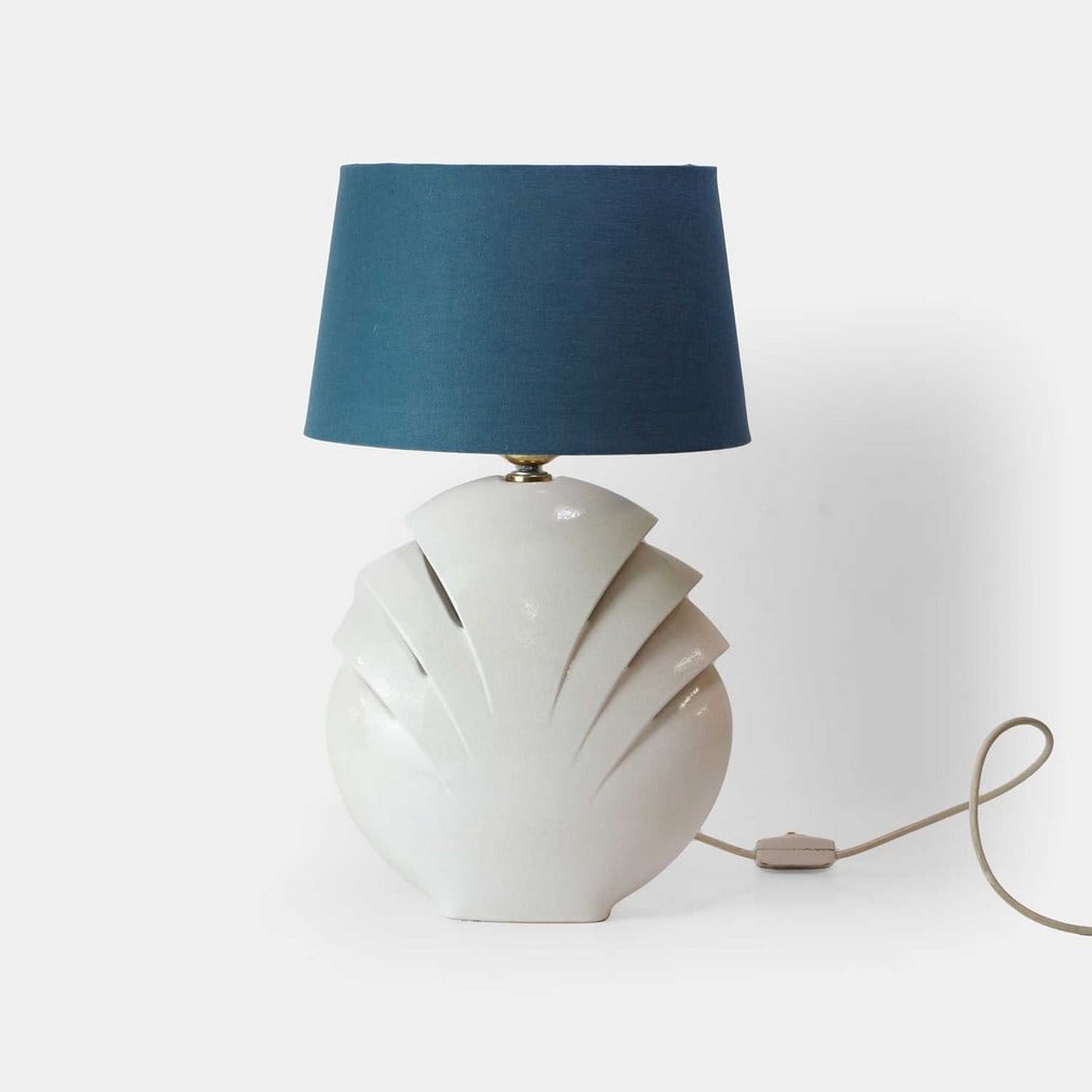 W Goebel KG, a ceramic table lamp,: W Goebel KG, a ceramic table lamp, circa 1970s, German, of shell form in a cream glaze, with a later blue fabric shade, with applied manufacturer's label (27cm wide, 14cm deep, 38.5cm high to