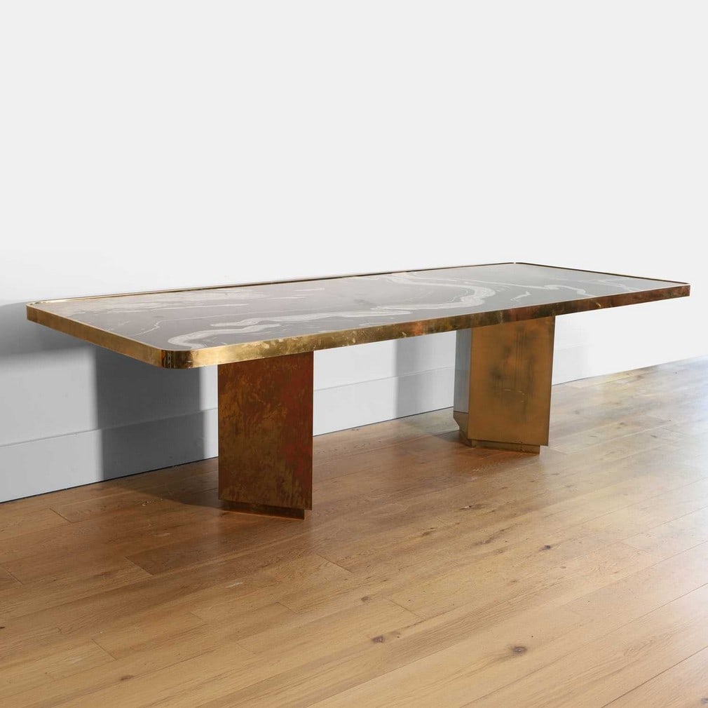 After Lara Bohinc, a dining table,: After Lara Bohinc, a dining table, circa 2000, the polished granite top encased within a gilded-brass mount, raised on twin diamond-form pedestals (275cm wide, 110cm deep, 76cm high) Provenance: