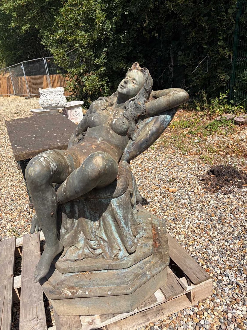 A bronze reclining nude female figure, modern,: A bronze reclining nude female figure, modern, modelled as a nude seated on a chair, with a jug and fish, raised on an octagonal plinth 98cm wide, 95cm deep, 120cm high Condition Report: With