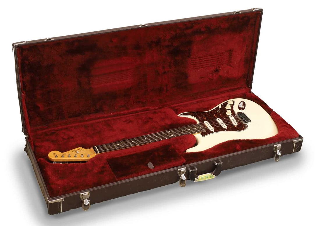 A 1999 Fender Stratocaster,: A 1999 Fender Stratocaster, Made in Mexico, the double cutaway body with an Olympic White finish and faux tortoiseshell pickguard, complete with hardcase, The pickups are, apparently, Bare Knuckle