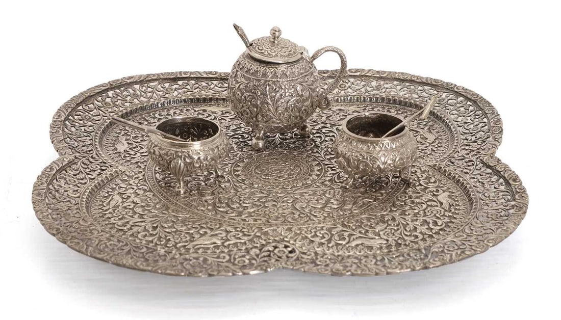 An Indian silver pierced quatrefoil shaped tray, late 19th century, Kutch,: An Indian silver pierced quatrefoil shaped tray, late 19th century, Kutch, profusely engraved with leaves and birds, on four paw feet, unmarked, tests silver, together with a three-piece condiment set