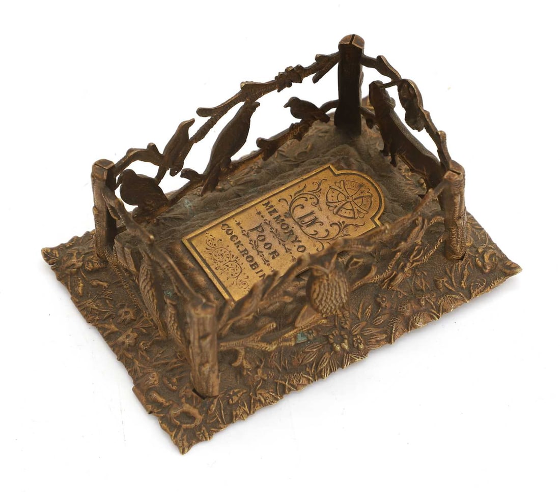 An Avery & Son Reddich needle case,: An Avery & Son Reddich needle case, modelled as Poor Cock Robin's Grave, the fencing modelled with mourning animals, the flat head stone lifting ot reveal a coffin, stamped mark to the base and