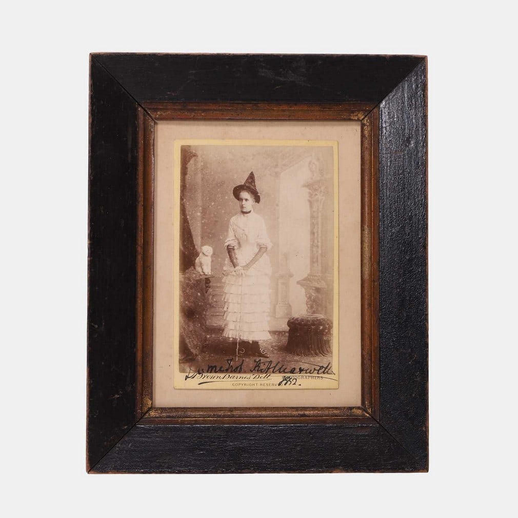 A Victorian photograph of a witch, dated 1882,: A Victorian photograph of a witch, dated 1882, the subject wearing a witch's hat, holding a cane, with a cat seated on a table beside her, a studio cabinet card photograph by Brown, Barnes & Bell Phot