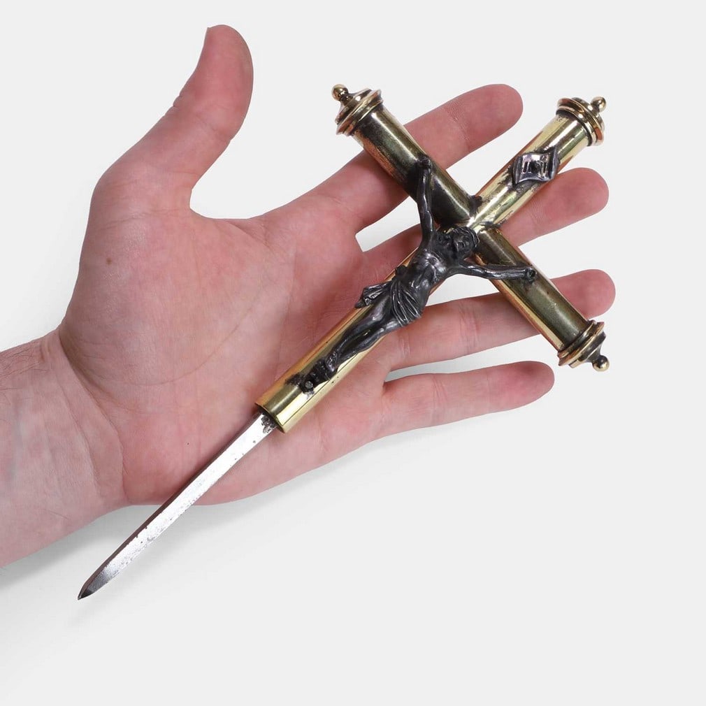 An unusual two-toned brass crucifix with a secret hidden dagger, 19th century,: An unusual two-toned brass crucifix with a secret hidden dagger, 19th century, with a silvered depiction of the suffering Christ, the top section lifts from the weighted base to reveal a concealed ste