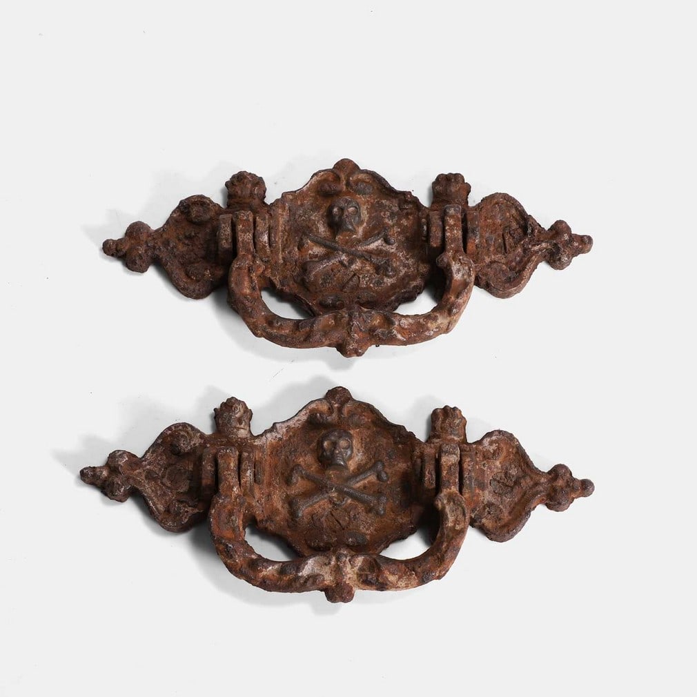 A pair of cast iron coffin handles, 19th century,: A pair of cast iron coffin handles, 19th century, each moulded with a skull and crossbones design (20.5cm wide, 9cm high) (2) Condition Report: Rust and age. Would make great drawer handles or door kn