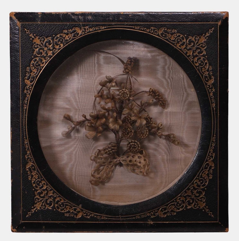 A rare and fine hairworked spray, circa 1860, probably American,: A rare and fine hairworked spray, circa 1860, probably American, the domed glazed top enclosing an elaborately woven spray of hair, backed by watered silk, in a gilt-leather embossed outer frame, with