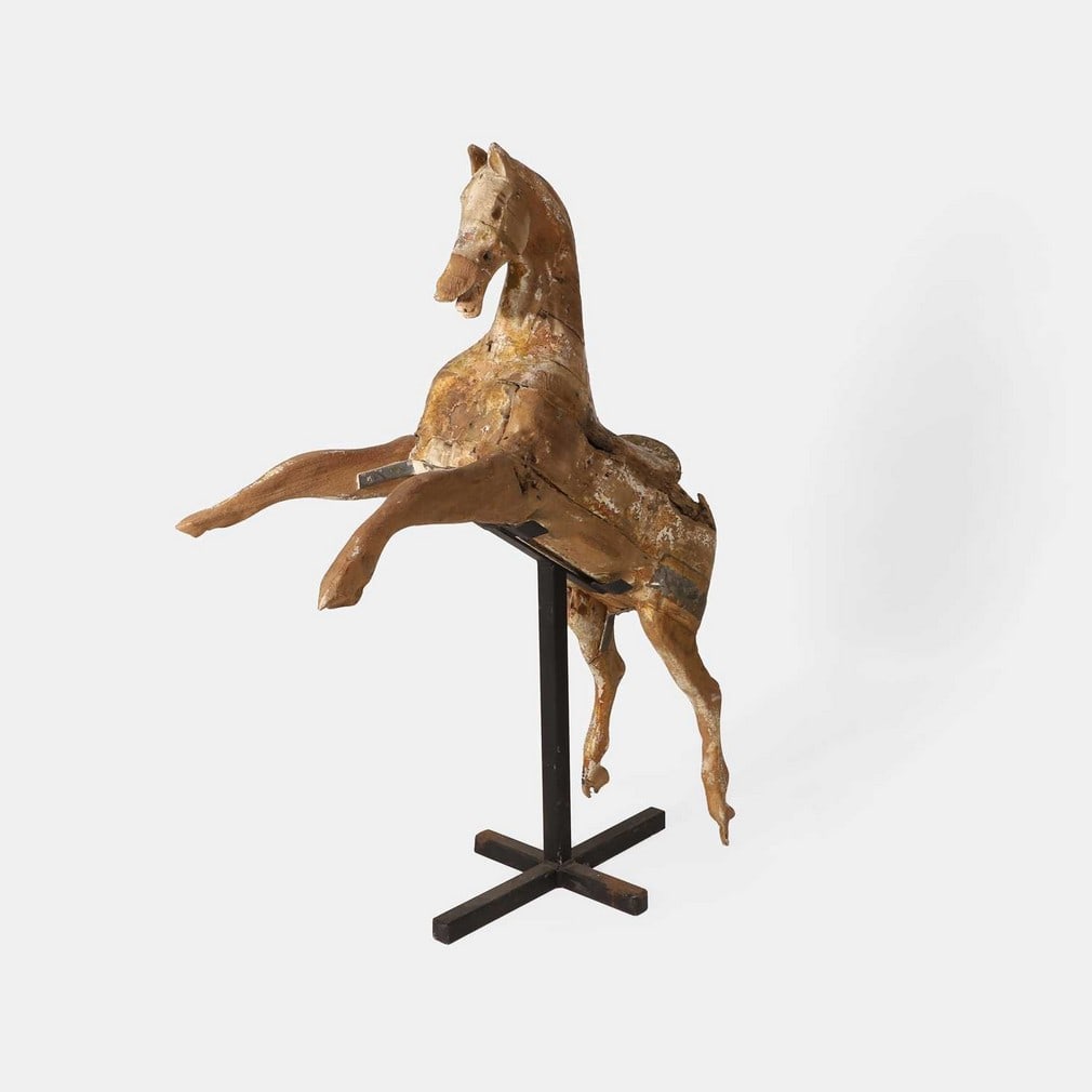 A naive carved wood galloper, circa 1890,: A naive carved wood galloper, circa 1890, with traces of original paint, raised on an iron stand (106cm long, 136cm high) (2)