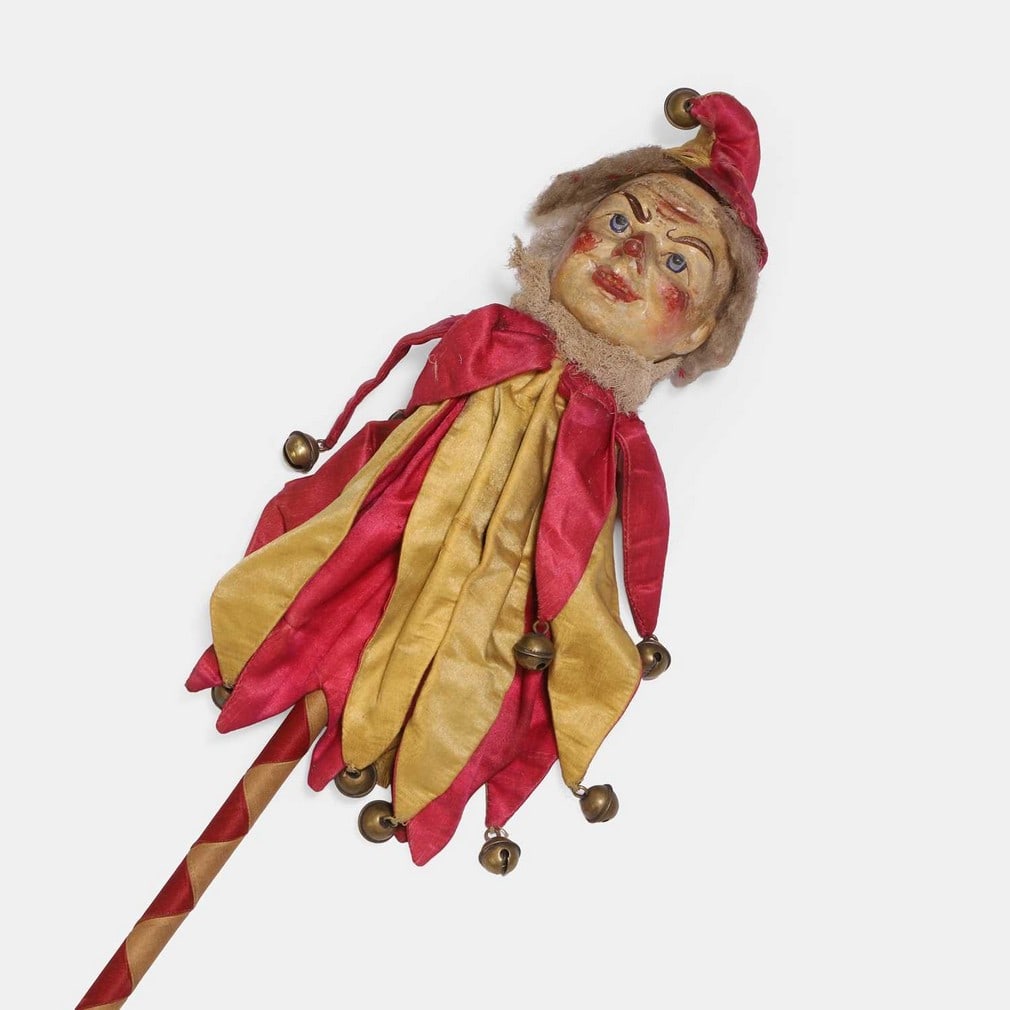 A marotte jester stick, late 19th century,: A marotte jester stick, late 19th century, carved and painted wood, with a gesso face, and a silk fabric body and hat with bells fixed to the ends, the shaft woven with silk (46cm long) Condition Repo