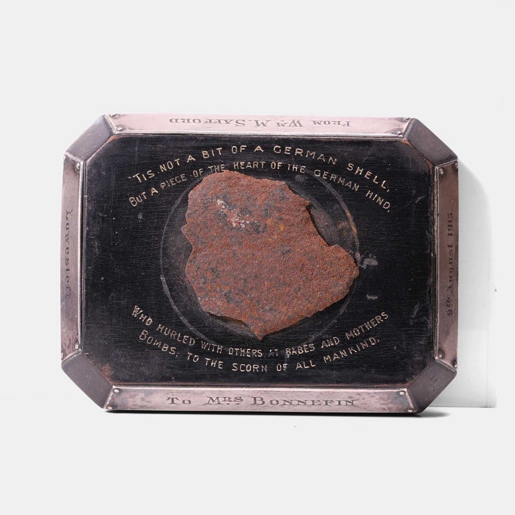 A First World War commemorative paperweight, commemorating the bombing of Lowestoft by the German: A First World War commemorative paperweight, commemorating the bombing of Lowestoft by the German Navy, on 9 August 1915, mounted with a shell fragment, on an ebonised plinth, inscribed 'Tis not a bit