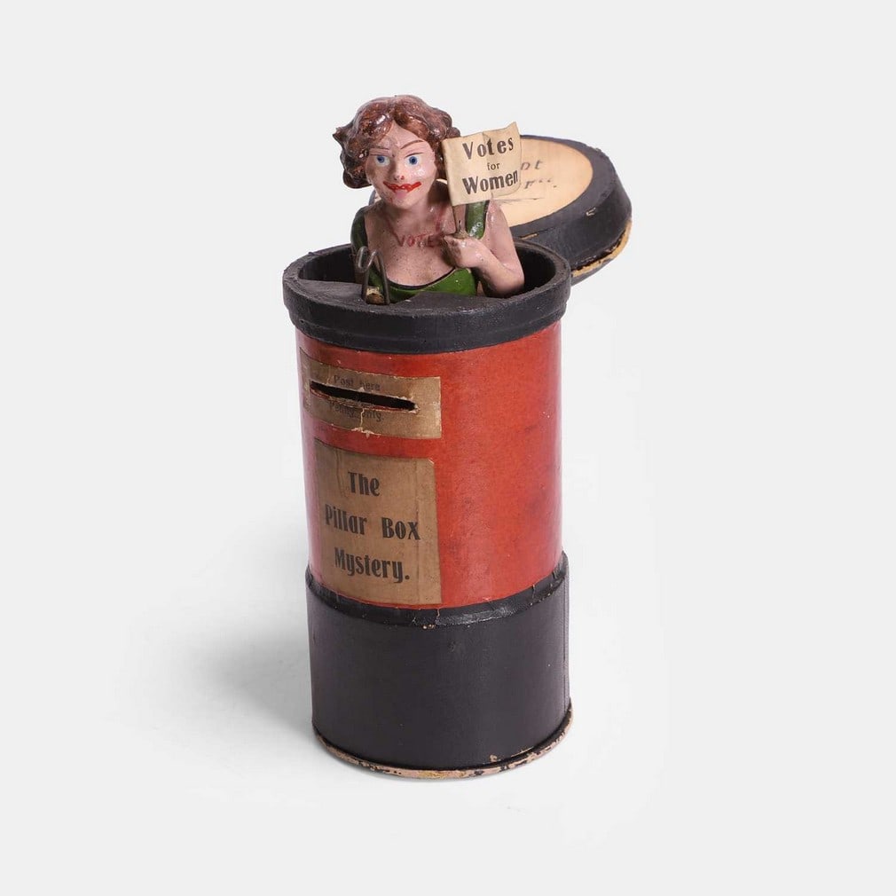 A rare suffragette letter-box money box, circa 1913, German,: A rare suffragette letter-box money box, circa 1913, German, the lid opening to reveal a spring-loaded painted figure of a suffragette, wearing a green dress and 'Votes' necklace, that emits a squeak,