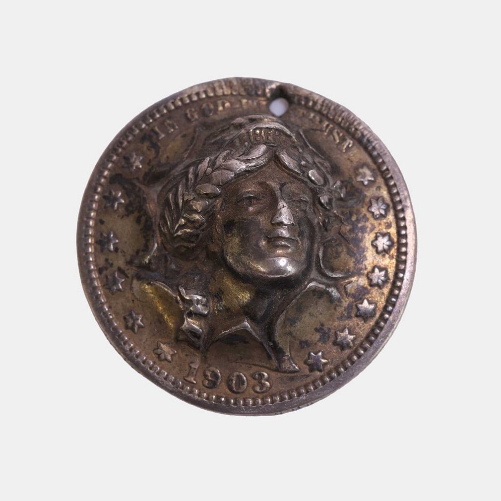 A three-dimensional American Quarter Dollar, dated 1903,: A three-dimensional American Quarter Dollar, dated 1903, the head of Liberty breaking through in very high relief, pierced as a pendant (2.5cm diameter) Condition Report: Bump to nose, pierced for nec