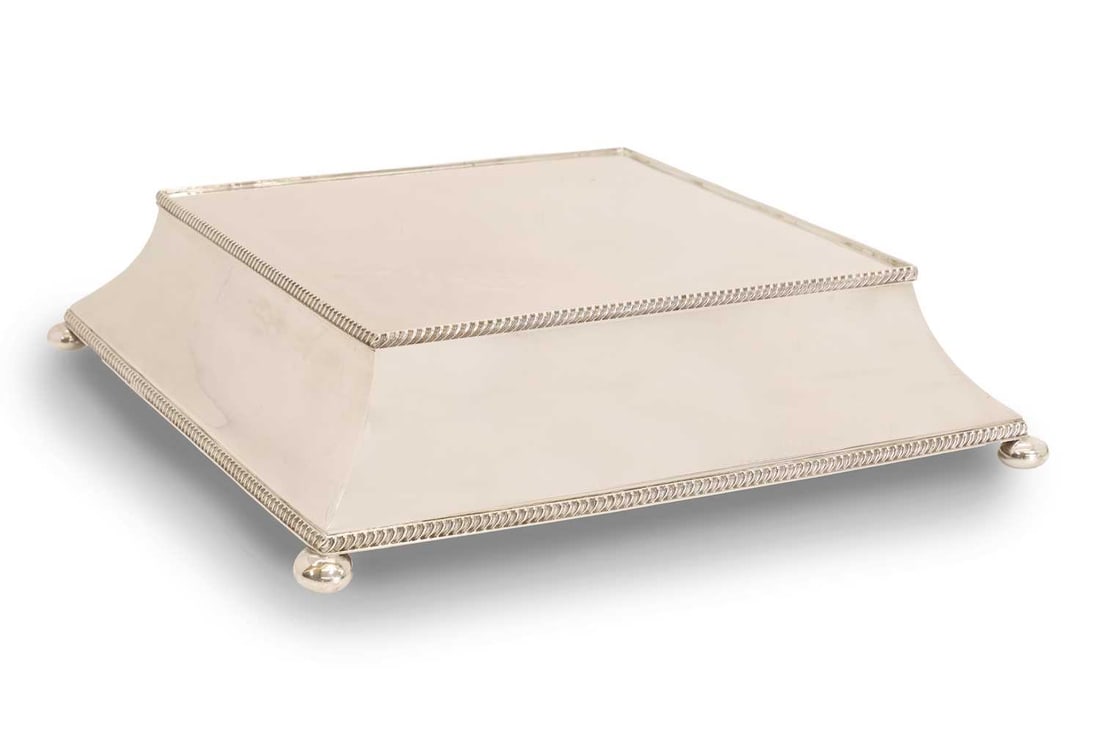 A silver-plated cake stand, 20th century,: A silver-plated cake stand, 20th century, the canted plinth, with gadrooned border, raised on ball feet. in a painted pine hinged box 48.5cm square, 12cm high 2 Condition Report: Fair overall.