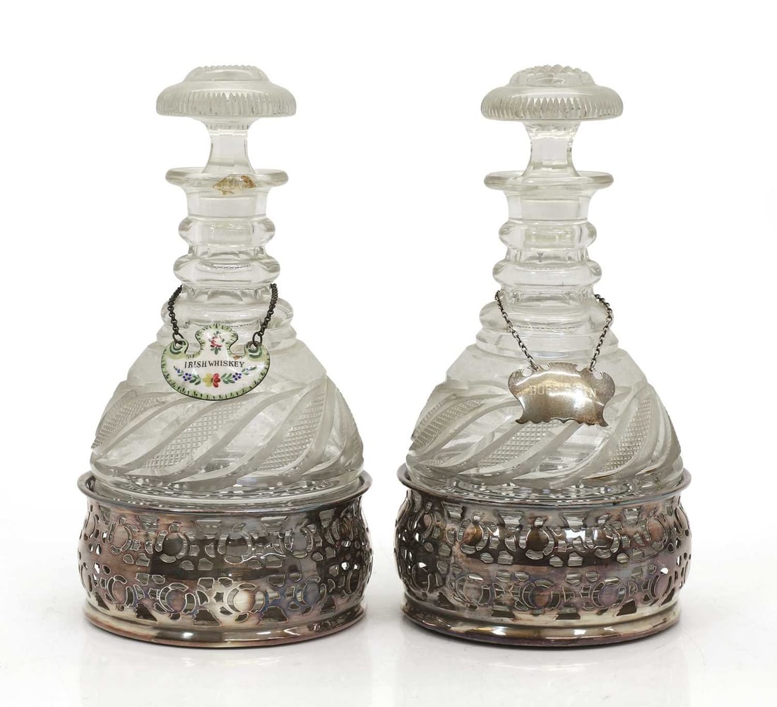 A pair of cut glass decanters, late 19th century,: A pair of cut glass decanters, late 19th century, of baluster form with mushroom stoppers, twsiting cut decoration, within silver plated bottle holders and enamelled labels 28.5cm high
