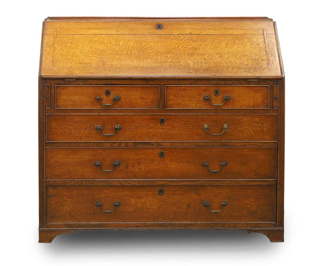 A George III oak bureau, early 19th century,: A George III oak bureau, early 19th century, with a low three-quarter gallery, the slope front over a fitted interior, centred with a cupboard and flanked with drawers and pigeon holes, over two
