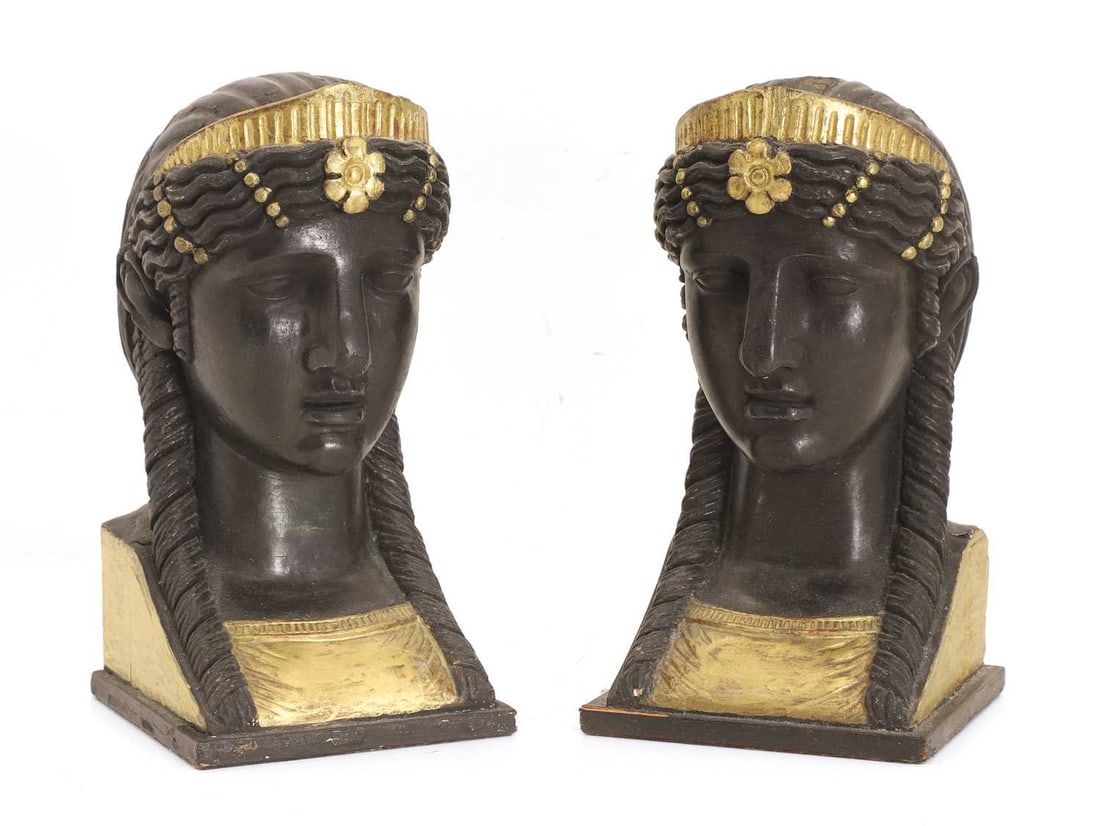 A pair of wooden Egyptian Revival sphinx-head bookends late 19th century,: A pair of wooden Egyptian Revival sphinx-head bookends late 19th century, finished in ebonised wood with gilt detailing, each carved and on a single square base, in black and gold Width 11.5cm, Depth