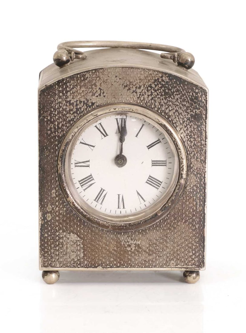 A silver table clock, 20th century,: A silver table clock, 20th century, by EM, London, 1906, with engine-turned design and arched top, the enamelled dial with Roman chapter ring 8cm wide, 6cm deep, 11cm high, total 19ozt