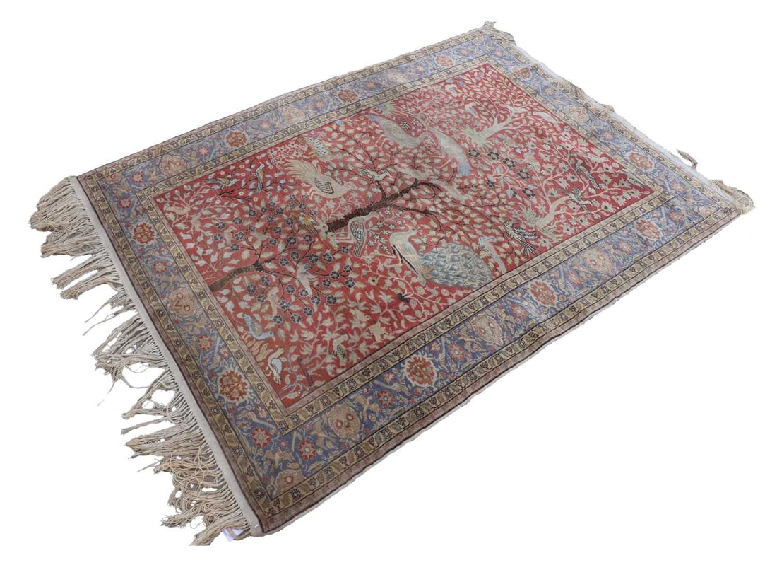 A Persian rug,: A Persian rug, tree of life decorated centre, on the red ground, the border with blue base and foliate design 125cm wide, 190cm deep Condition Report: Faded in colour. Silk blend. Tassels long and