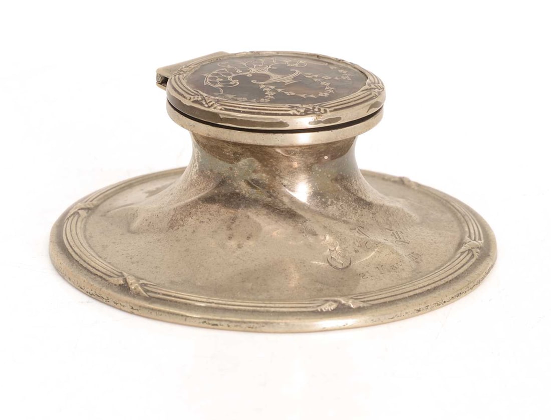 A silver and tortoiseshell inkwell,: A silver and tortoiseshell inkwell, the top inlaid with urn and swags, initialled and dated, the base filled 10.7cm wide, 5cm high, total 8.5ozt