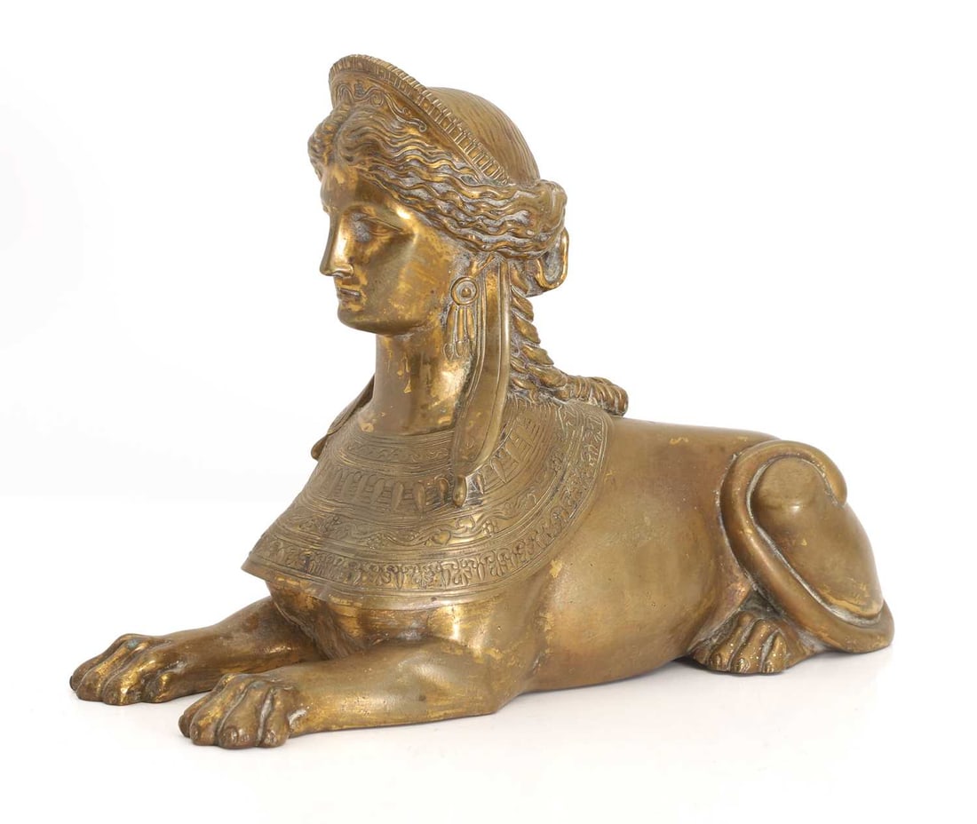 A brass Egyptian Revival sphinx, late 19th century,: A brass Egyptian Revival sphinx, late 19th century, in seated position, with forward set paws Width 31.6cm, Depth 10.4cm, Height 21.7cm,