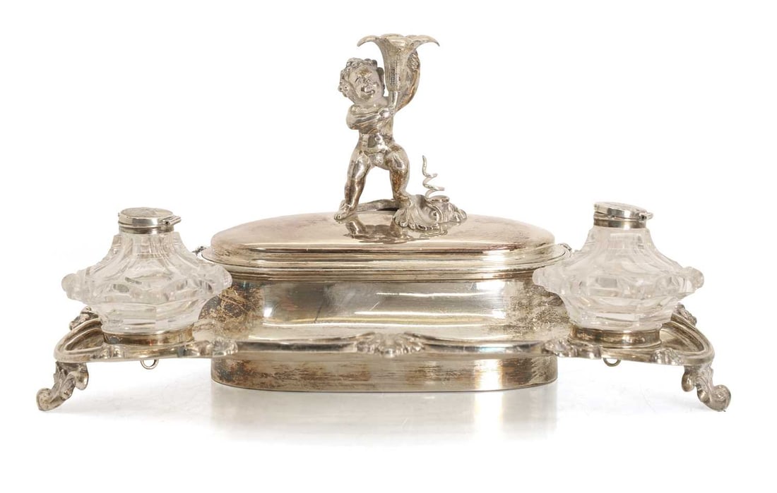 An Elkington & Co, silverplated ink stand,: An Elkington & Co, silverplated ink stand, with two glass reserves and a cherub holding a flower, surmounting the lid, the interior is comprised of three sections 32cm wide, 17cm high