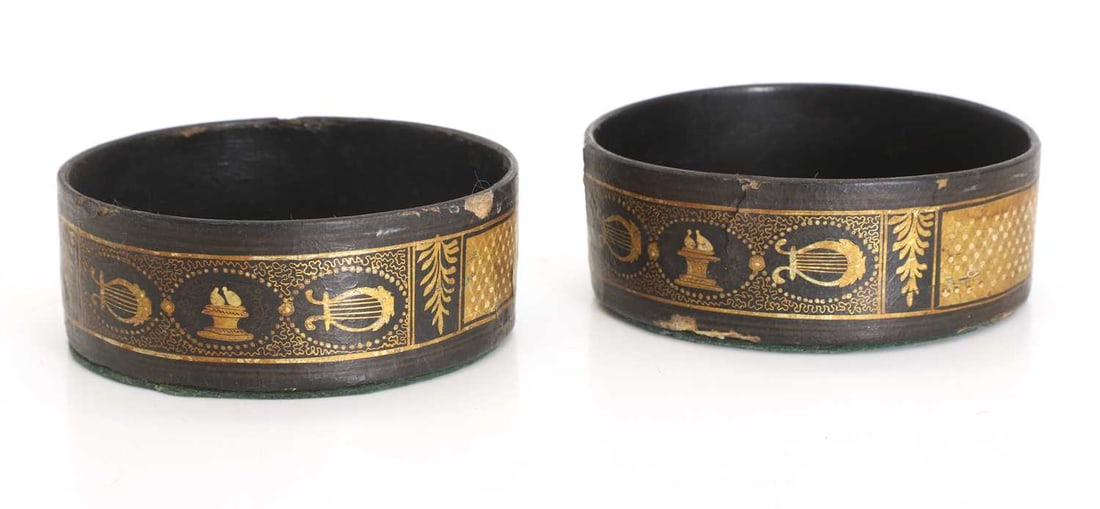 A pair of black japanned bottle coasters,: A pair of black japanned bottle coasters, of circular form with gilt detailing and harp, floral and trellis pattern exterior 12.5cm wide, 5cm high 2 Condition Report: Knocks and losses to the sides.