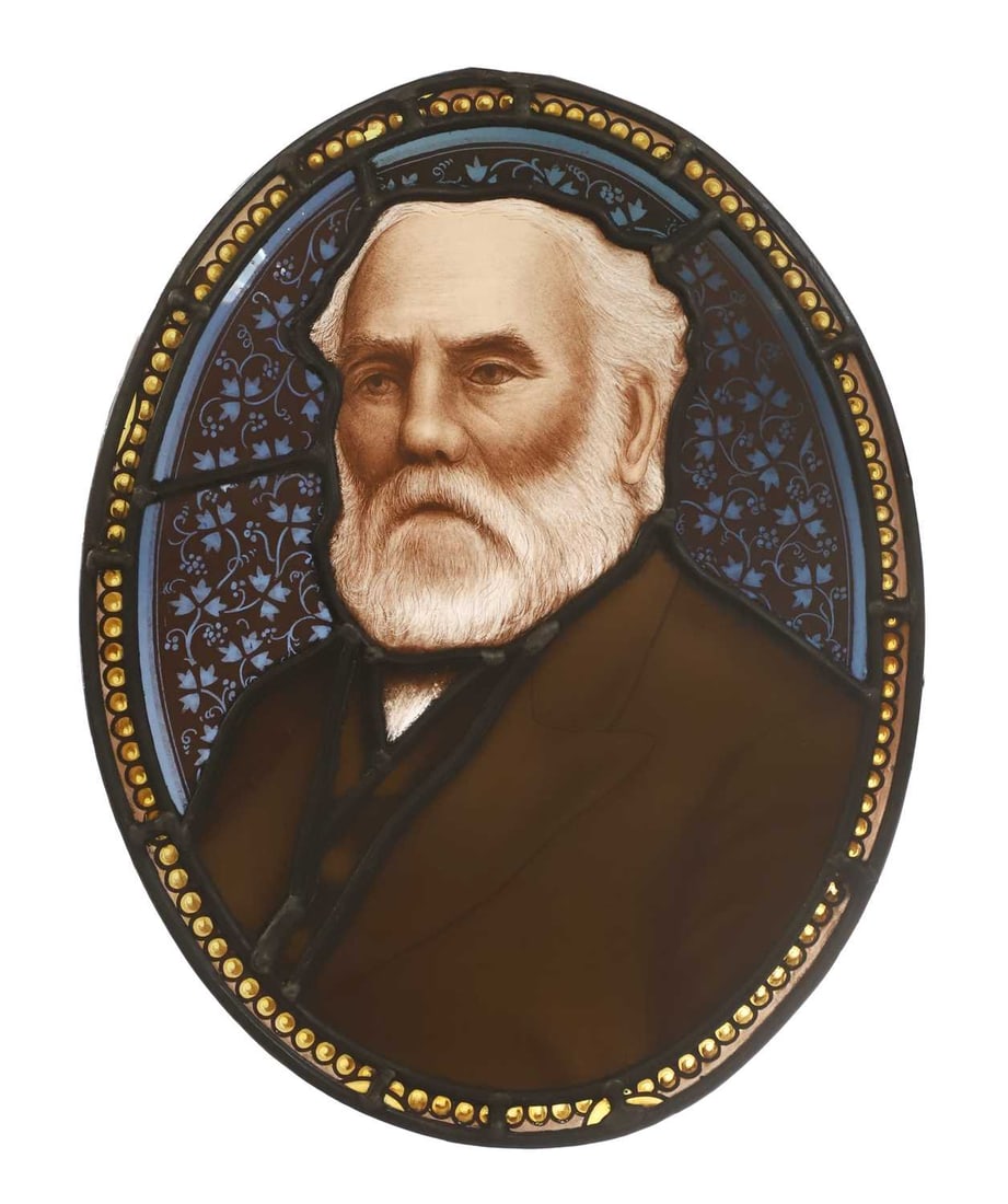 A pair of stained glass panels, late 19th century,: A pair of stained glass panels, late 19th century, both of oval form, the centres of each with a portrait, one of a bearded gentleman, the other of a woman wearing glasses, within decorated glass