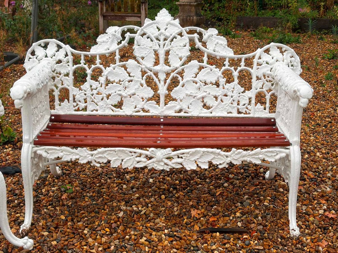 A cast iron garden bench, in the manner of Coalbrookdale,: A cast iron garden bench, in the manner of Coalbrookdale, cast back and sides with trailing branches and oak leaves, the arms terminating in dog's head finials above a later slatted seat, raised on