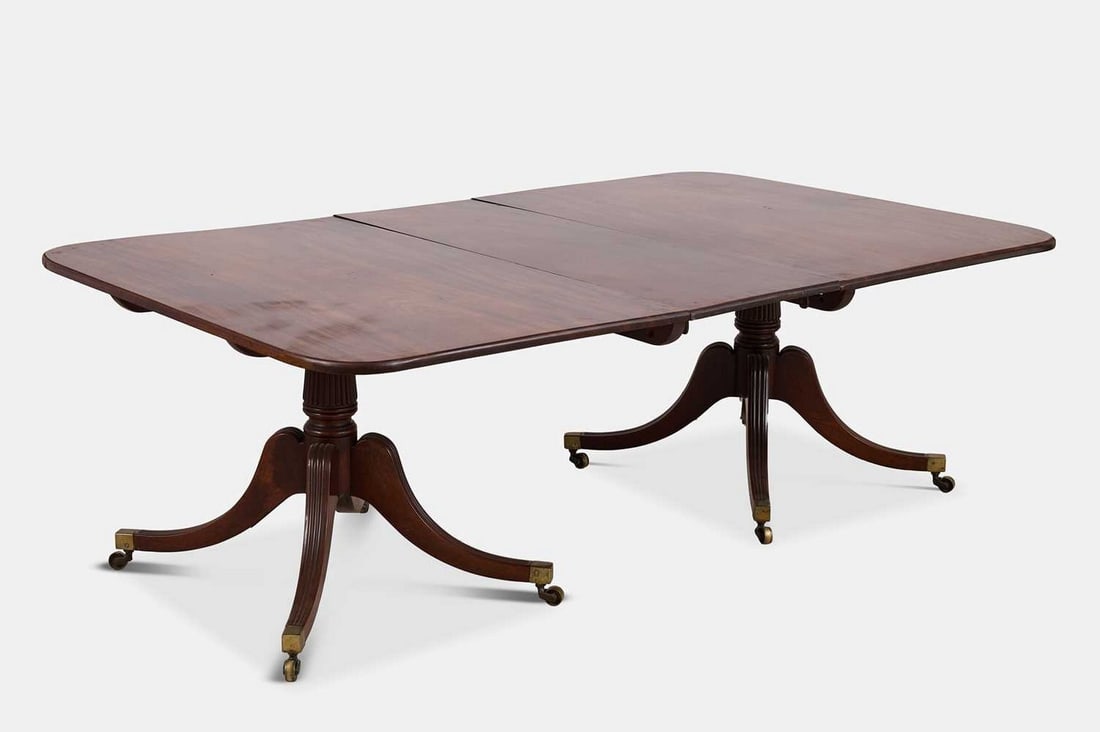 A Regency mahogany twin-pedestal dining table, circa 1815,: A Regency mahogany twin-pedestal dining table, circa 1815, the rounded rectangular top raised on outswept reeded supports, terminating in brass caps and castors (221cm wide, 135cm deep, 72cm high) Pro