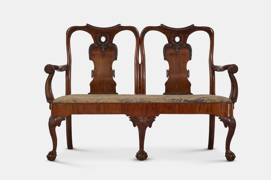A George II mahogany chair-back settee, circa 1740 and later, possibly Irish,: A George II mahogany chair-back settee, circa 1740 and later, possibly Irish, each 'chair' with a flared top rail over a vasiform splat decorated with laurel wreaths, above a wide drop-in seat with ne