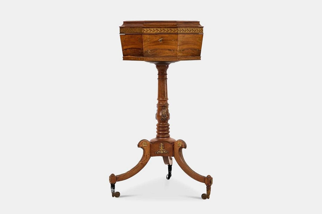 A Regency rosewood and brass teapoy, circa 1820,: A Regency rosewood and brass teapoy, circa 1820, of sarcophagus form, the octagonal hinged lid enclosing a velvet-lined fitted interior with two cut-glass mixing pots, raised on a turned baluster colu