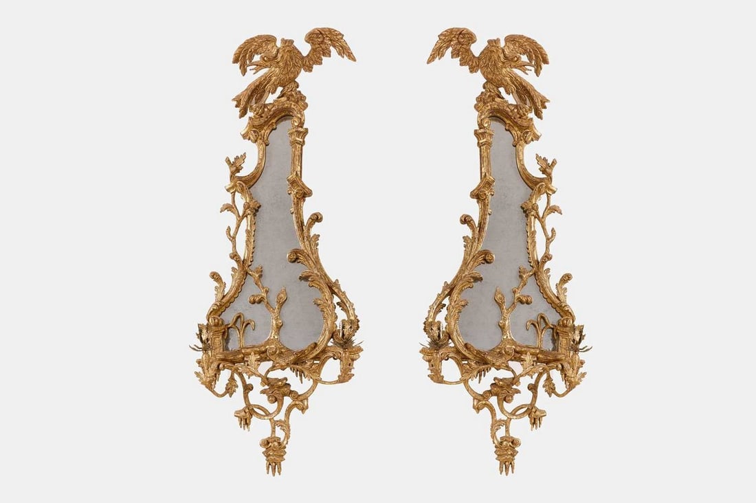 A pair of George III-style giltwood girandoles, late 19th/early 20th century, in the manner of: A pair of George III-style giltwood girandoles, late 19th/early 20th century, in the manner of Thomas Chippendale, in the rococo taste, each shaped plate enclosed within a scrolling foliate frame, sur