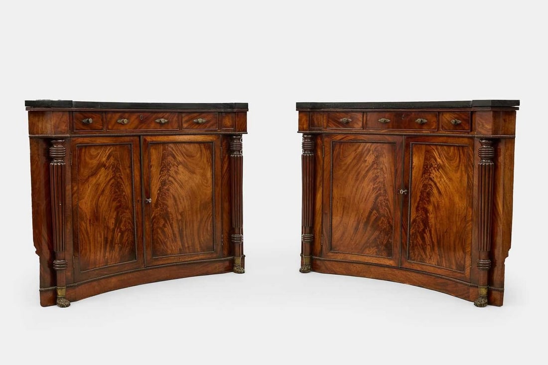 A pair of Regency mahogany corner cabinets, circa 1815,: A pair of Regency mahogany corner cabinets, circa 1815, each of concave form, with three drawers over cupboard doors enclosing a shelved interior, flanked by tapering reeded columns terminating in paw