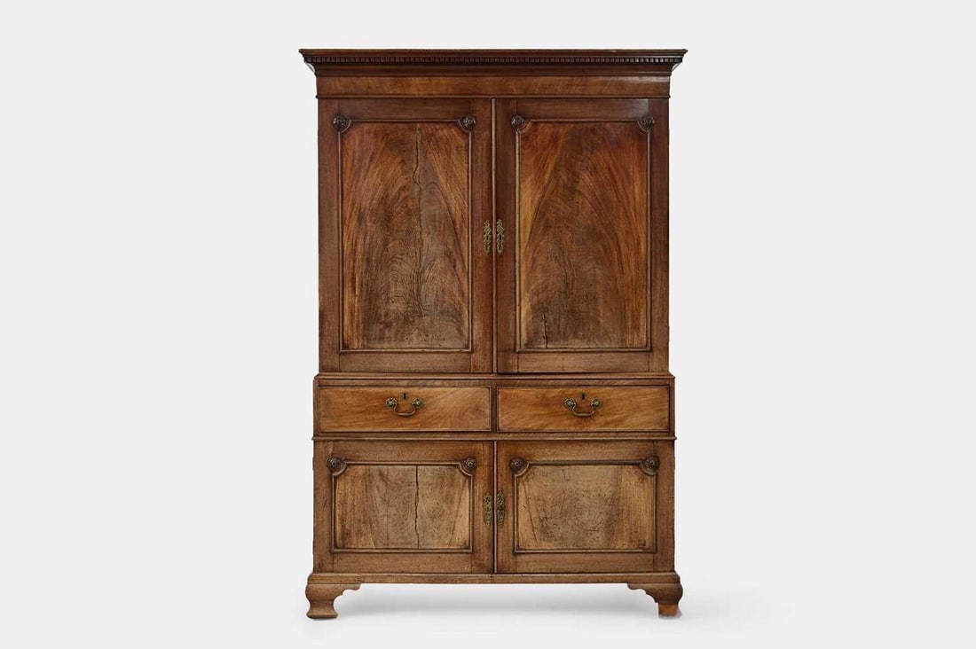 A George III mahogany linen press, third quarter of the 18th century,: A George III mahogany linen press, third quarter of the 18th century, the projecting dentil-moulded cornice above a pair of panelled doors decorated with rosette roundels, the doors enclosing slides, 