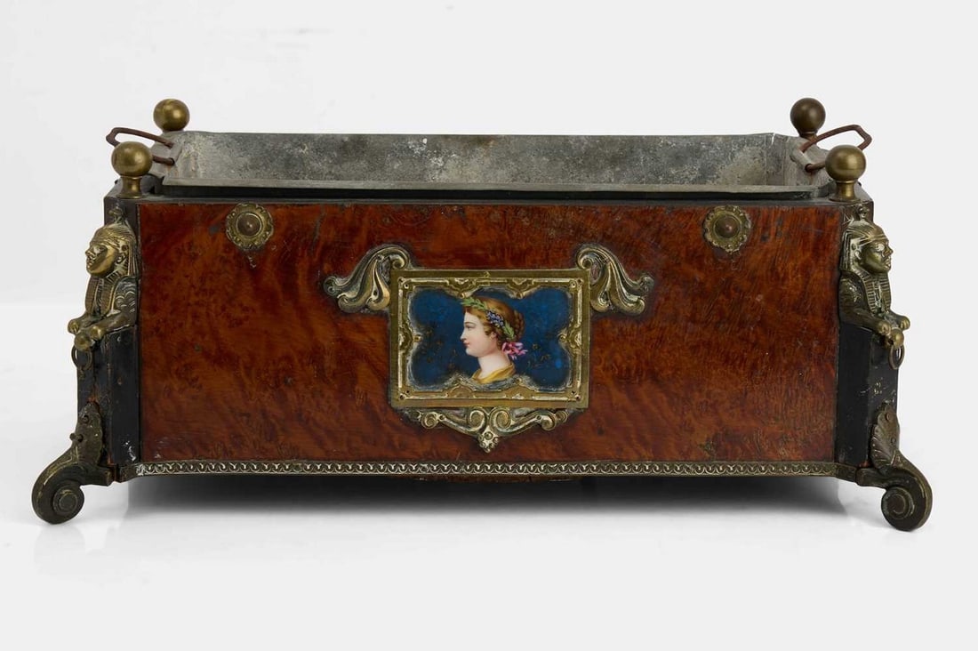 A Napoleon III walnut and gilt-metal jardinière, third quarter of the 19th century,: A Napoleon III walnut and gilt-metal jardinière, third quarter of the 19th century, fitted with lion mask handles, the body centred on either side by an enamelled portrait of a lady, raised on sphinx