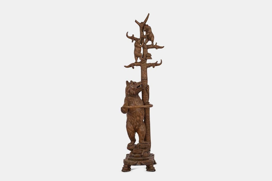 A Black Forest carved wooden hall stand, early 20th century, Swiss,: A Black Forest carved wooden hall stand, early 20th century, Swiss, in the form of a large bear against a tree, with a pair of smaller bears climbing the branches, on a naturalistic rockwork base with