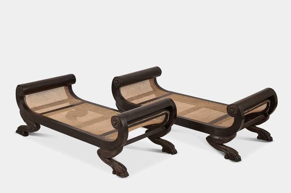 A pair of carved ebony stools, mid-19th century, Anglo-Ceylonese,: A pair of carved ebony stools, mid-19th century, Anglo-Ceylonese, each sectional caned seat enclosed within a scrolling reeded frame decorated with floral roundels, raised on outscrolling paw feet (14