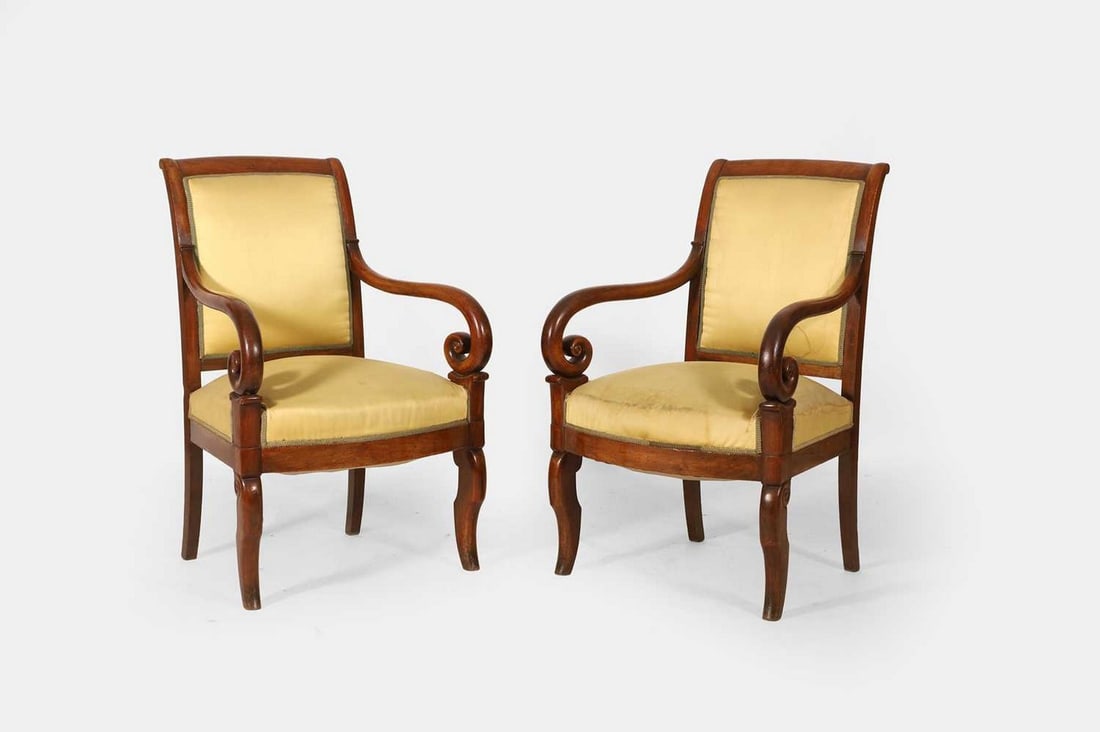 A pair of Empire-style mahogany-framed armchairs, late 19th/early 20th century,: A pair of Empire-style mahogany-framed armchairs, late 19th/early 20th century, each covered in antique gold upholstery, the wide stuffover seat flanked by downscrolling arms, raised on sabre legs (57