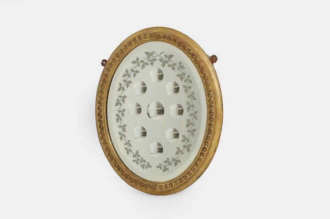 A sorcerer's mirror, 19th century,: A sorcerer's mirror, 19th century, the oval mirror plate set with nine roundels, enclosed within a giltwood frame decorated with a repeating foliate border (44cm wide, 3.5cm deep, 53cm high) Condition