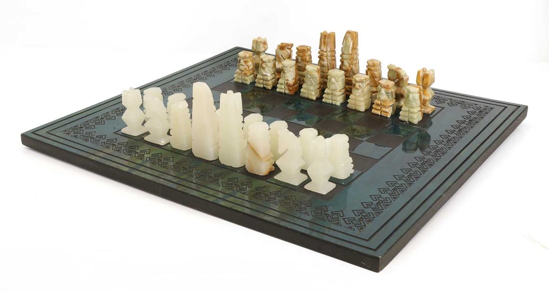 An Aztec style calcite and onyx chess board, late 20th century,: An Aztec style calcite and onyx chess board, late 20th century, on a green and ebonsided wooden board, a full set of pieces, made in Mexico 58cm wide, 52cm deep