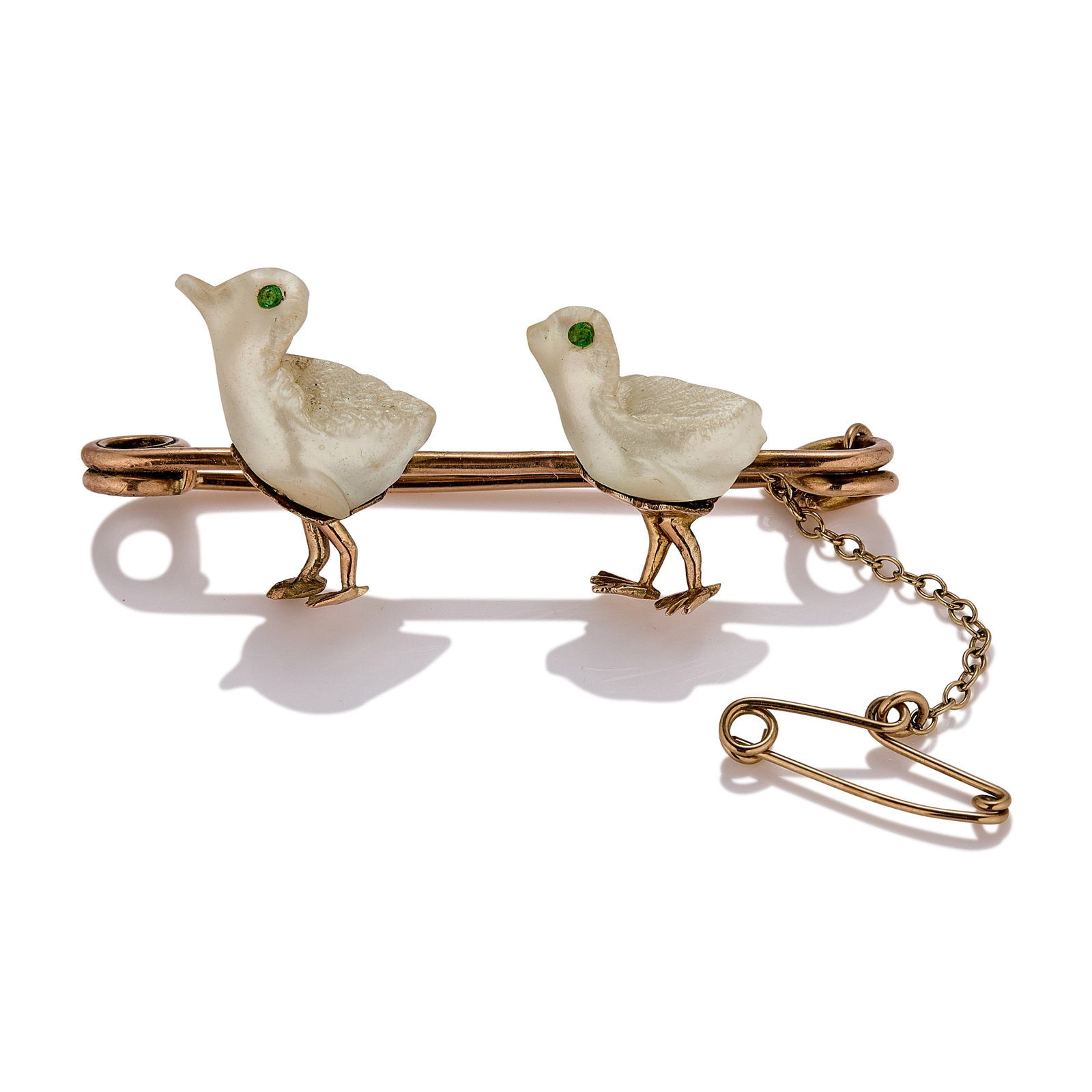 An antique mother-of-pearl novelty brooch,: An antique mother-of-pearl novelty brooch, designed as two carved mother-of-pearl chicks with faceted emerald eyes, upon a pin brooch, tested as approximately 9ct gold (Length 4.5cm; 4.8g) Condition