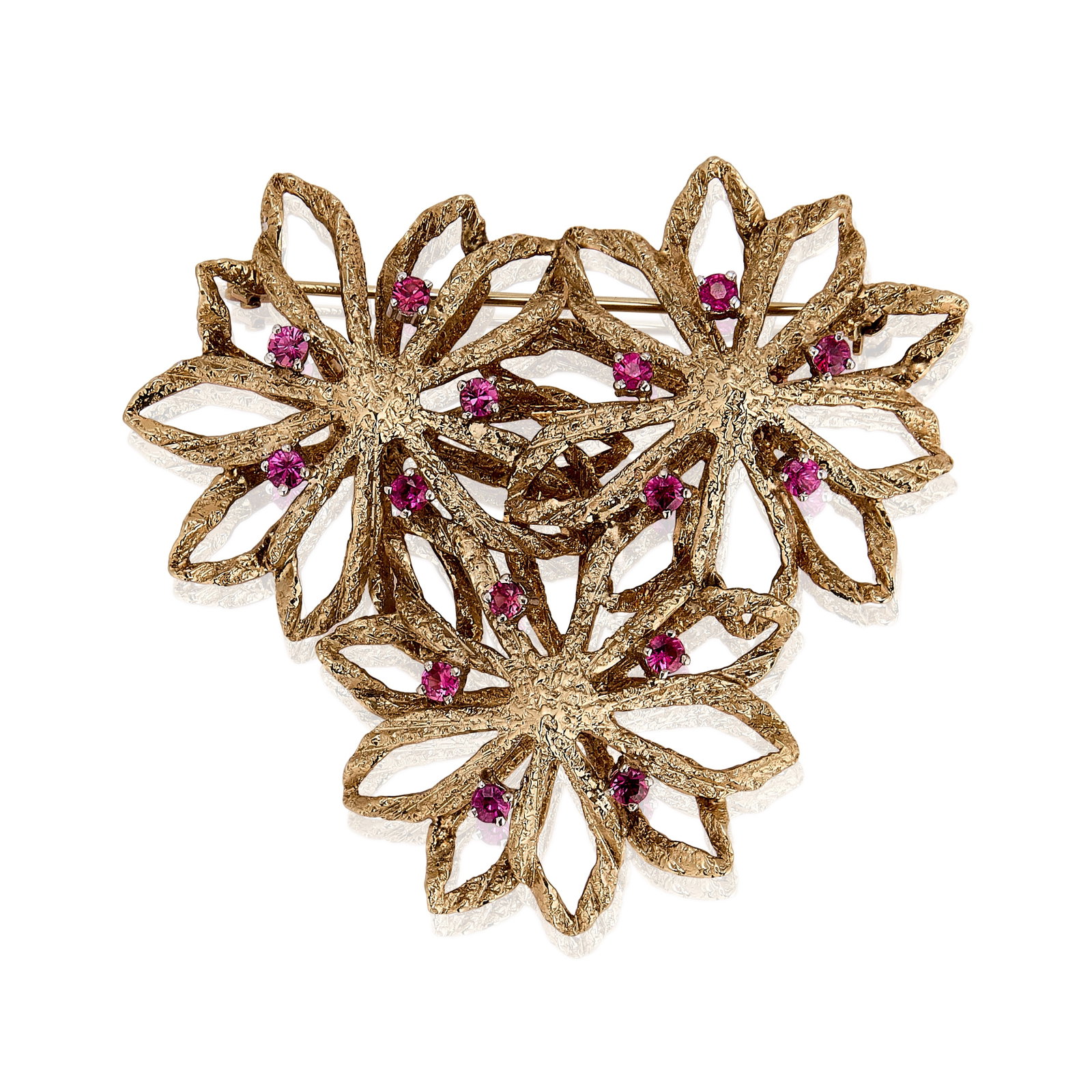 A 9ct gold ruby set floral brooch, circa 1970,: A 9ct gold ruby set floral brooch, circa 1970, composed of three openwork flowerheads with a textured finish and accented with circular cut rubies, London import hallmark 1970 (Width 5cm; Length