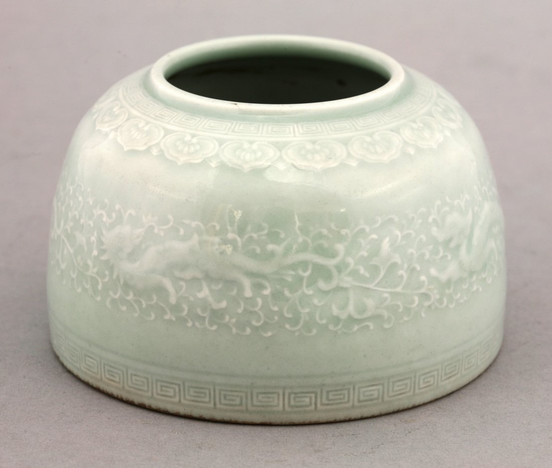 A celadon Water Pot, post-1950, finely moulded with: A celadon Water Pot, post-1950, finely moulded with dragons amongst spuming waves, between ruyi and key fret borders, six character seal mark of Yongzheng, 6cm