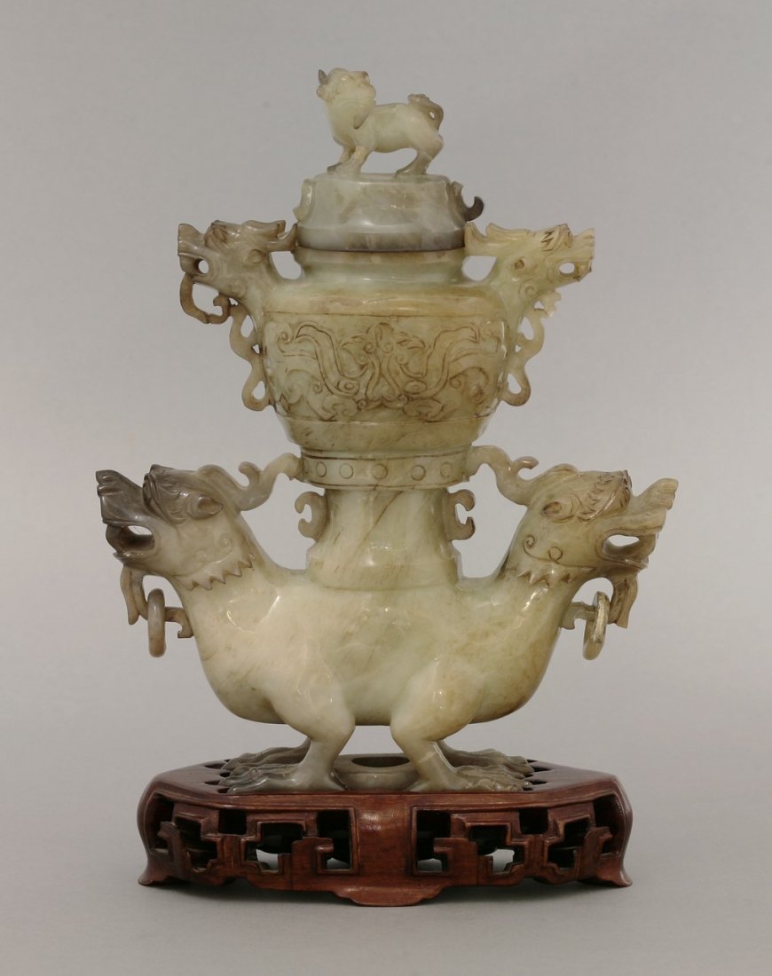 A complex grey-green stone Carving, modern, in the form: A complex grey-green stone Carving, modern, in the form of an archaic vase and cover with dragon head handles and knop, supported on the back of two further dragons, loose ring handles, tiny chips, 20