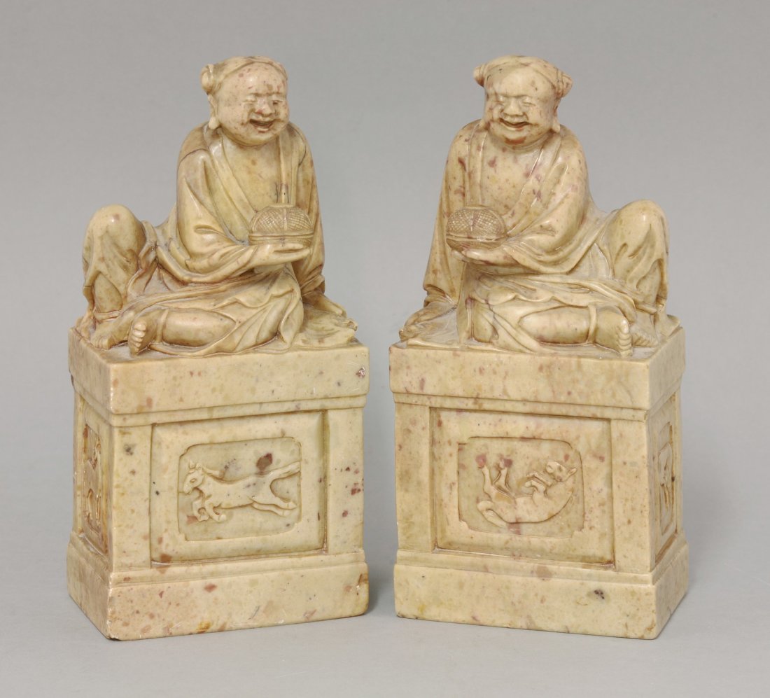 A pair of Chinese soapstone Bookends, early 20th: A pair of Chinese soapstone Bookends, early 20th century, each carved as an Immortal with a bowl on a high plinth, a horse on each face, 22cm (2) The figures could represent Mu Wang, famed for his hor