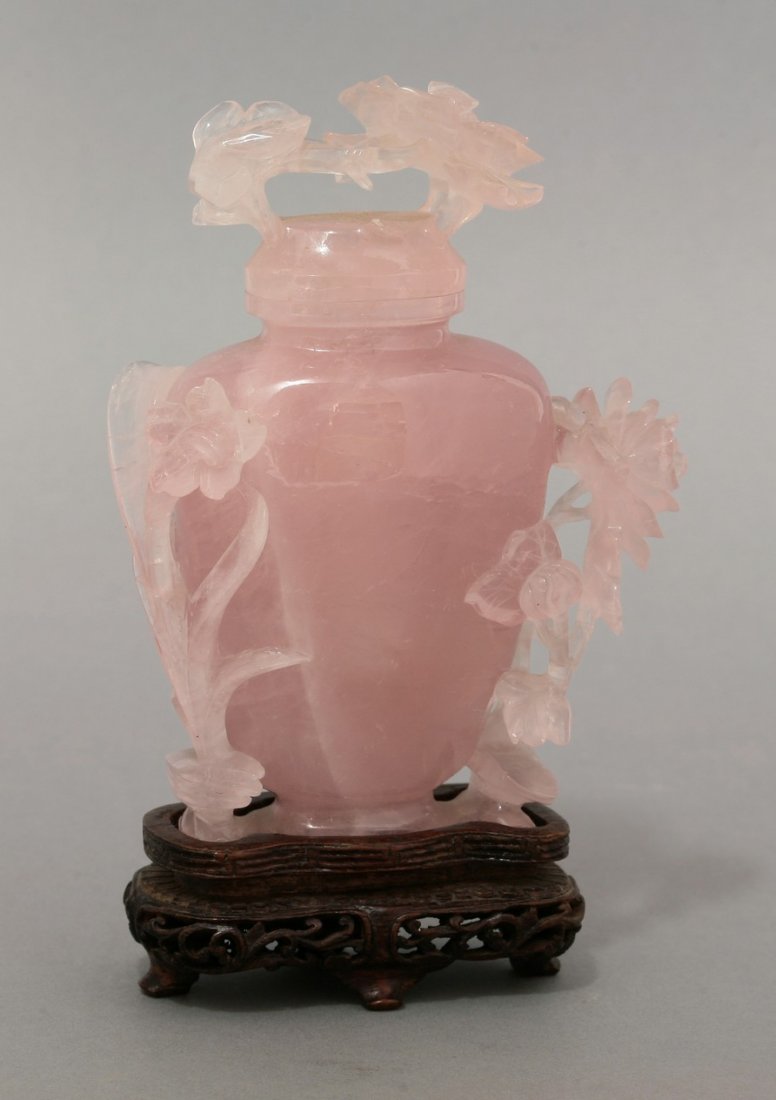A rose quartz Vase and Cover, 1950s, the shield-shaped: A rose quartz Vase and Cover, 1950s, the shield-shaped body with high relief peony and leaves, the pink stone suffused with white, minor chips, 12.5cm, fitted wood stand, box