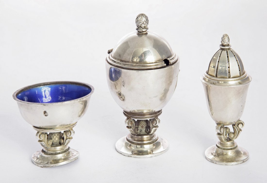 A Danish metalwares three-piece acorn pattern condiment: A Danish metalwares three-piece acorn pattern condiment set, by Georg Jensen, with import marks for London 1963, designed by Johan Rohde, comprising a salt and mustard with enamelled blue interiors an