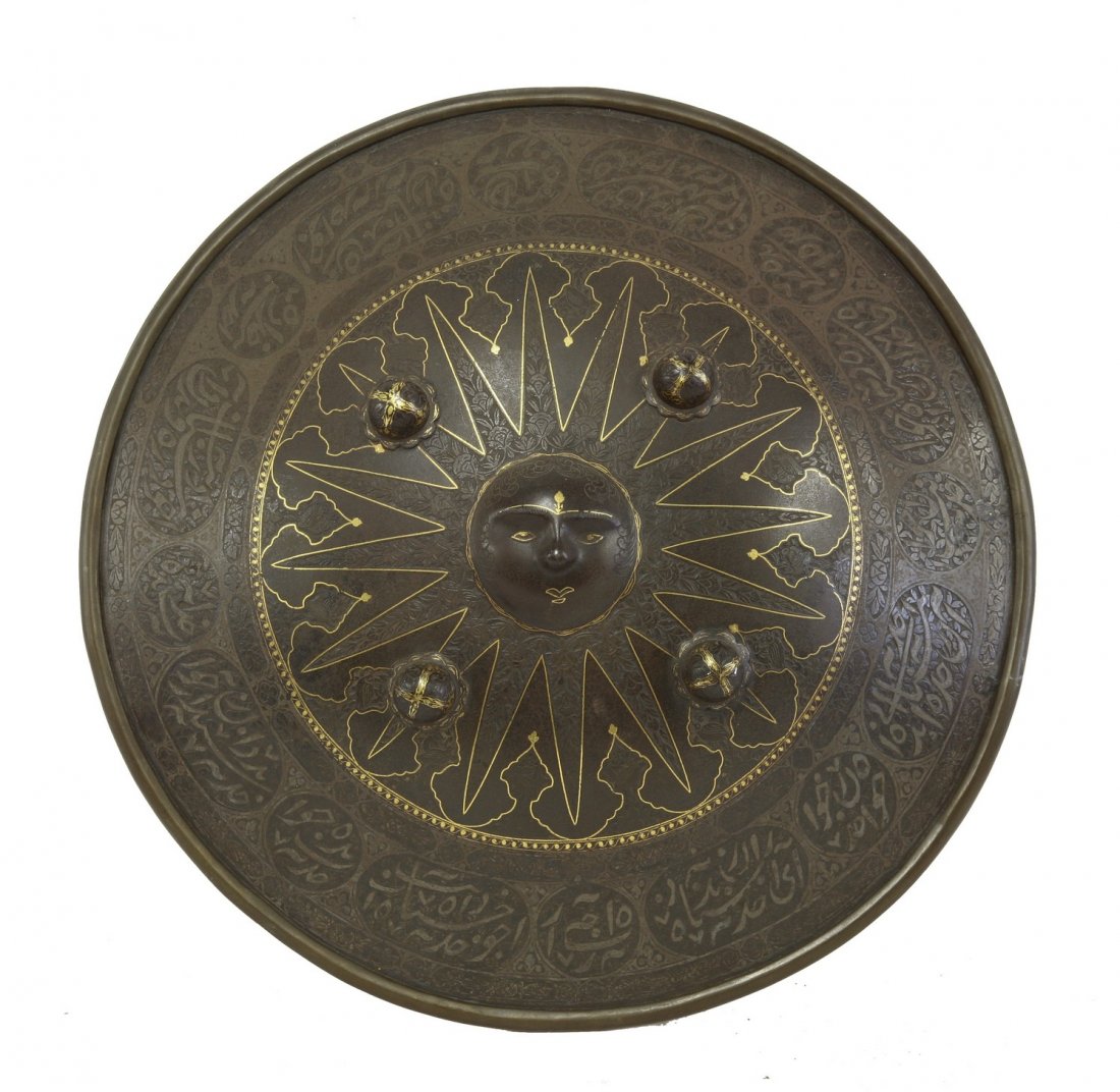A dhal or shield, Indian or Persian, damascened, with: A dhal or shield, Indian or Persian, damascened, with inlaid gilt lining and inscriptions in compartments, four small bosses and a central mask boss, 45cm diameter