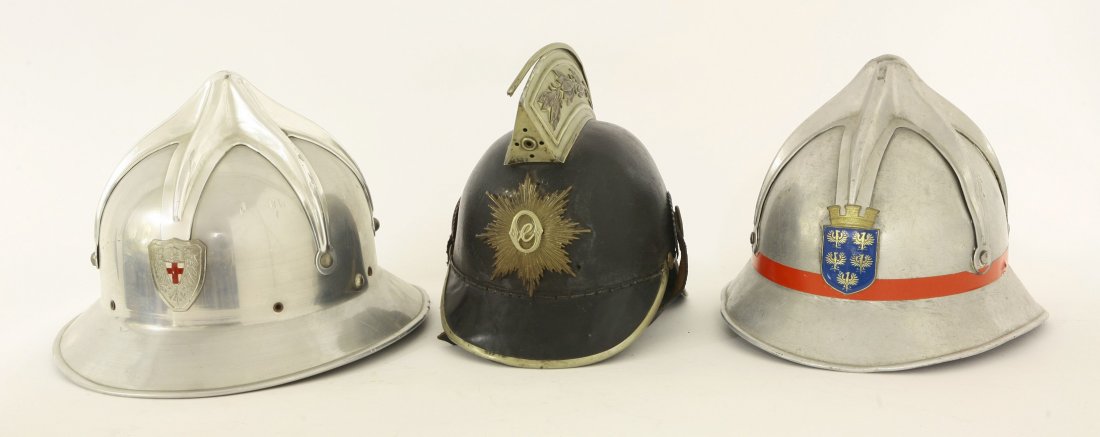 Three Austrian fire helmets, one leather and brass with: Three Austrian fire helmets, one leather and brass with ornate comb and cocades to sides, together with two later officers' helmets, all complete with chinstraps and liners (3)