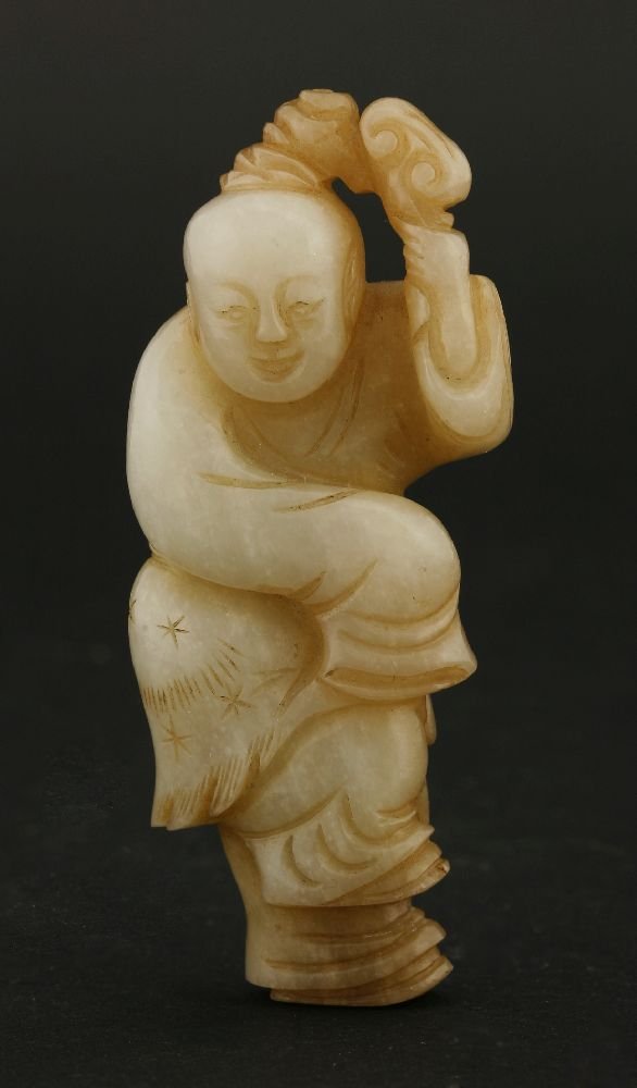 A jade Carving of a boy,Song/Yuan dynasty (960-1368),: A jade Carving of a boy,Song/Yuan dynasty (960-1368), one foot raised, one arm hidden beneath a long sleeve, the other holding a lingzhi above his head, the stone white and honey coloured, paper label